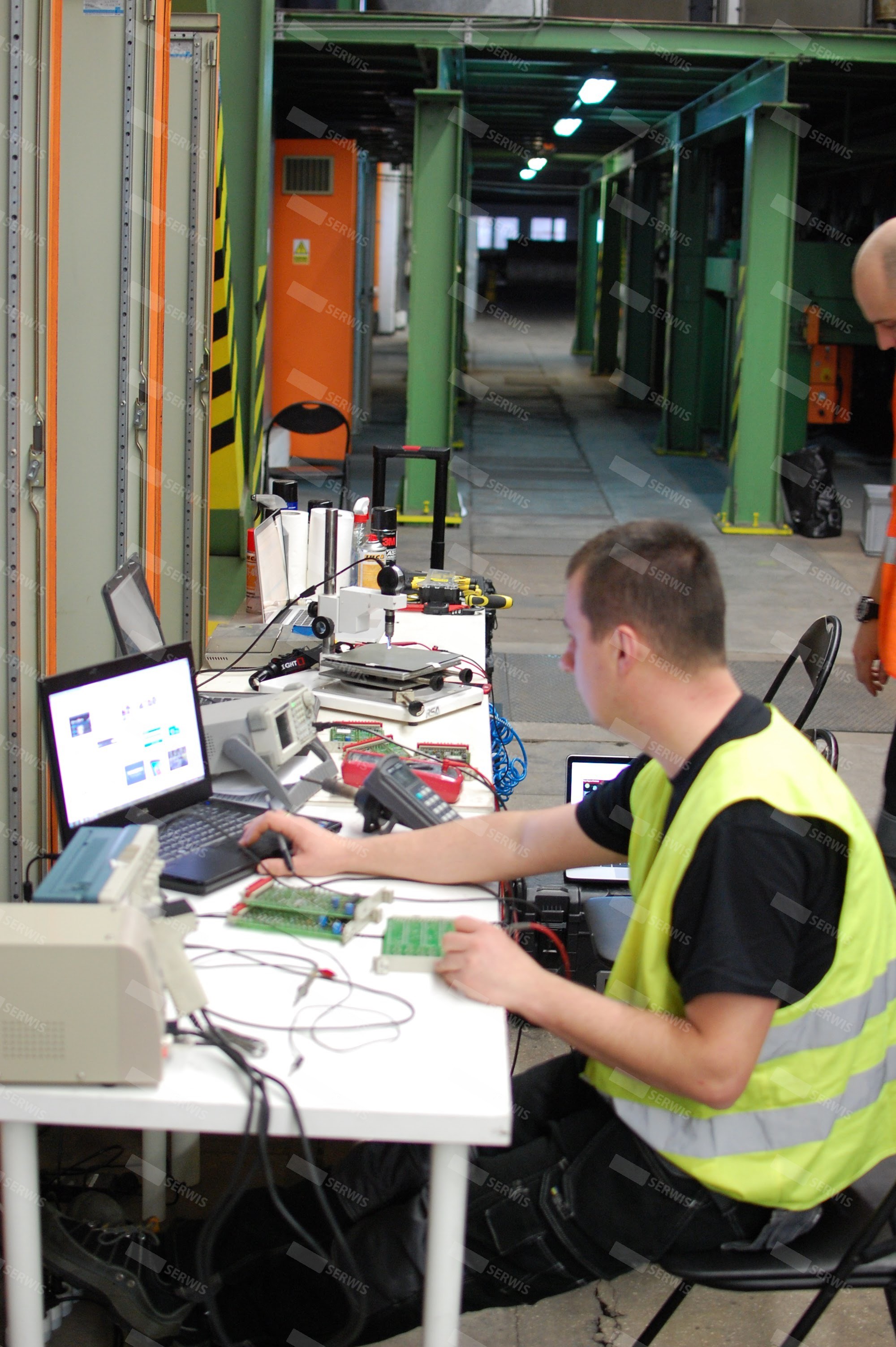 Technik w kamizelce odblaskowej testujący elektronikę na laptopie w warsztacie
