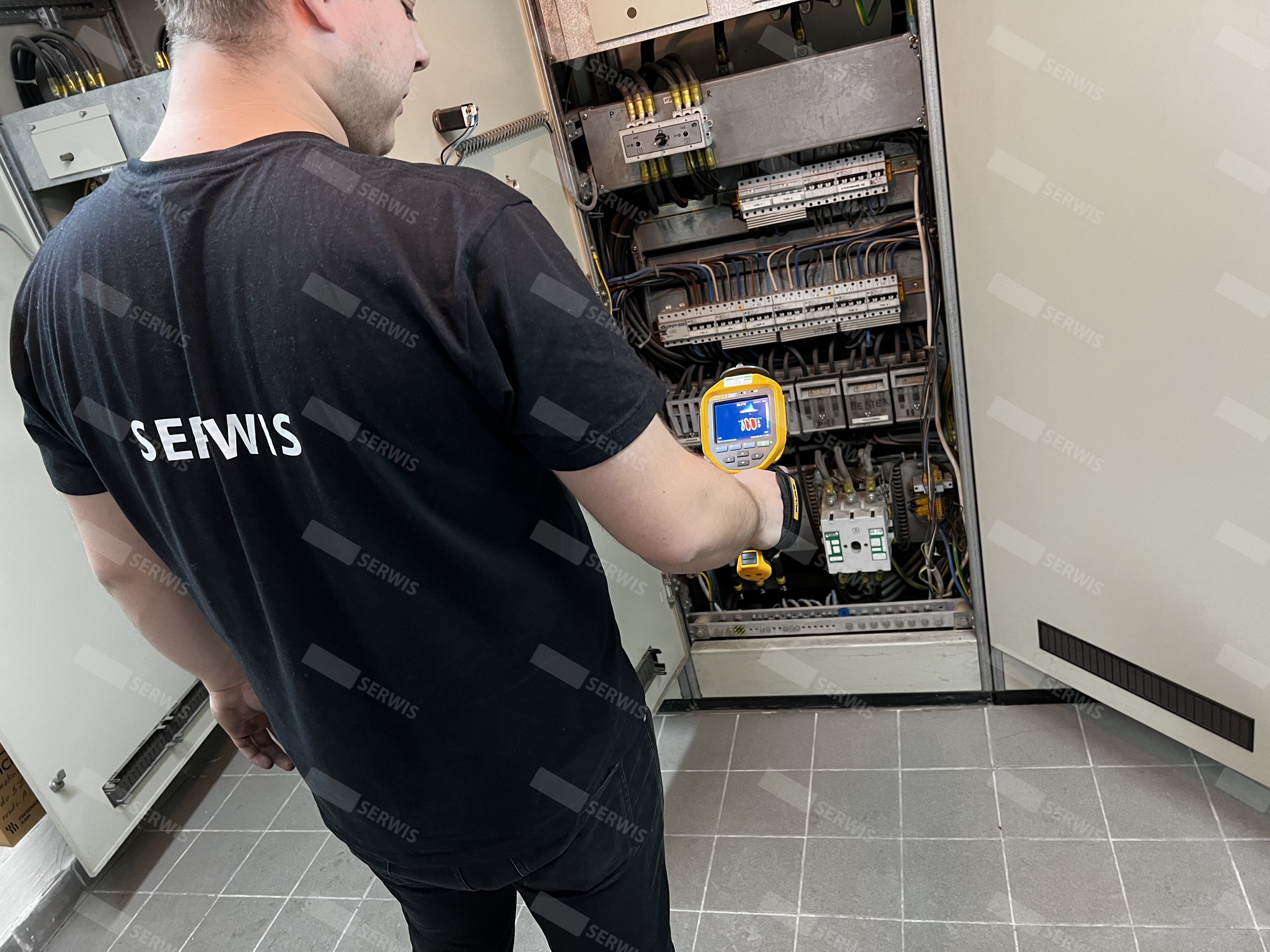 Technik serwisowy przeprowadzający przegląd szafy sterowniczej za pomocą miernika