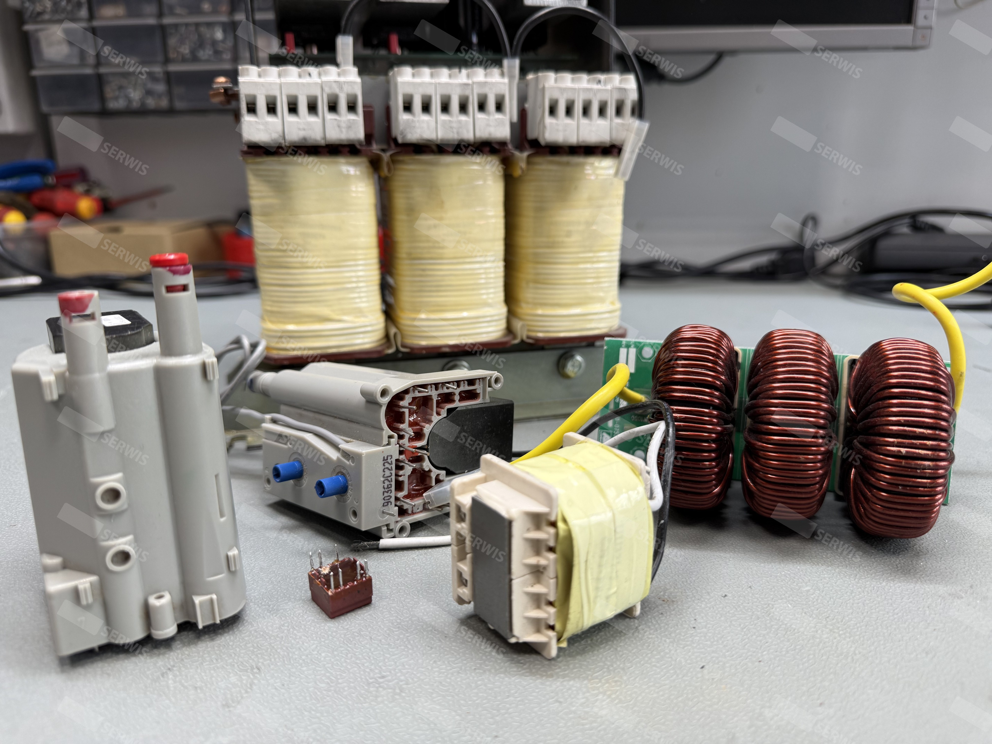 Różnorodne cewki, dławiki i transformatory na stole warsztatowym, używane w elektronice.