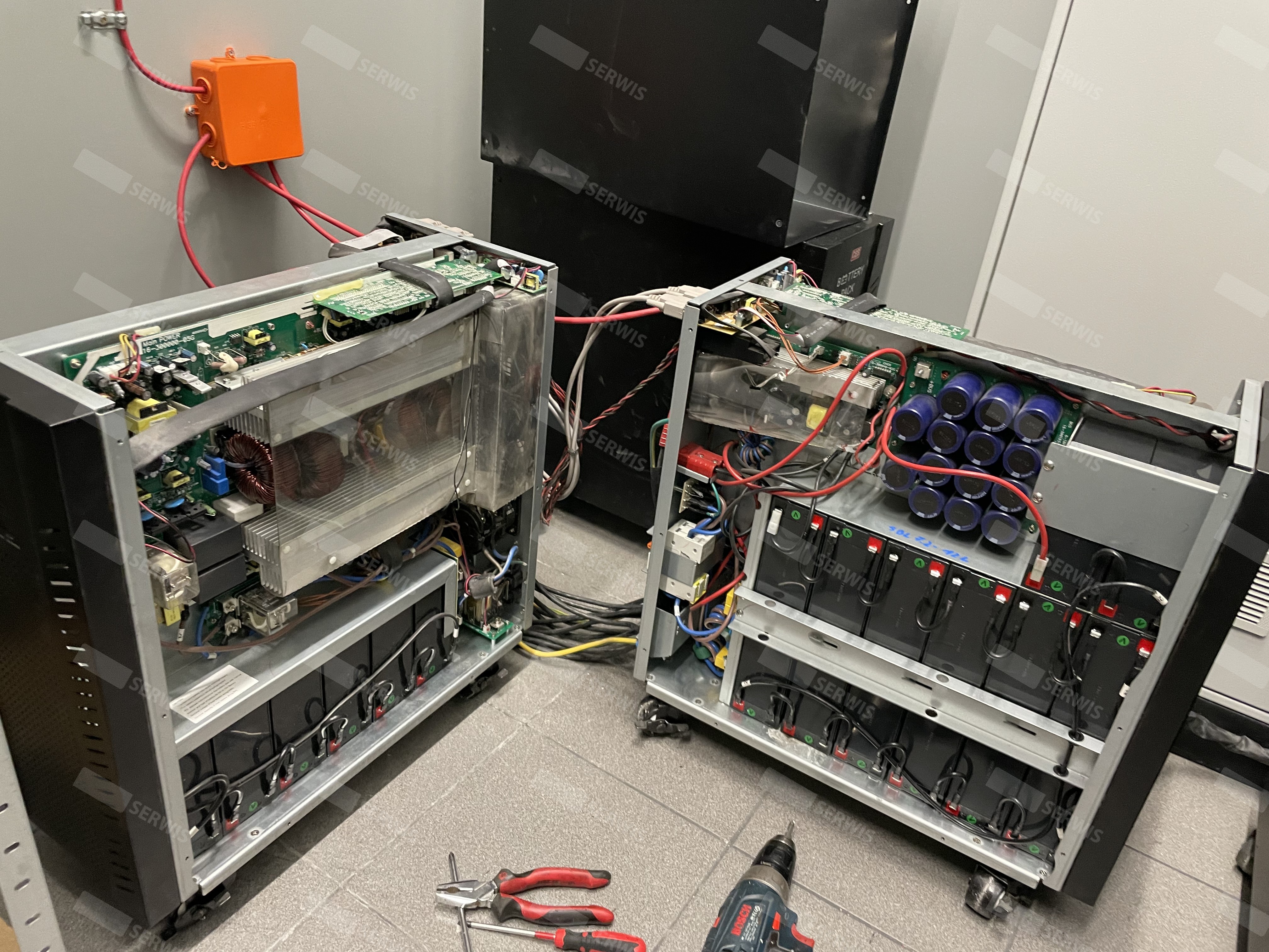 Otwarte obudowy UPS podczas przeglądu serwisowego z widocznymi podzespołami i narzędziami.