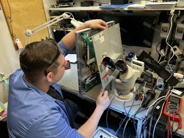 Technik serwisowy naprawiający komputer przemysłowy przy użyciu mikroskopu